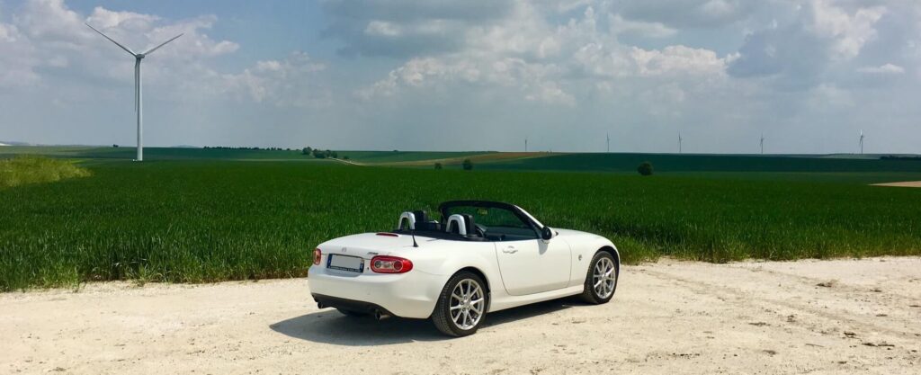 White Mazda NC Miata in front of fields and windmills