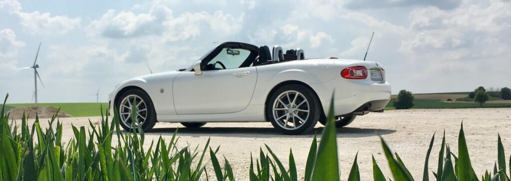 White Mazda NC Miata behind grass